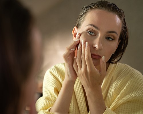 Woman looking in mirror, concerned about wrinkles