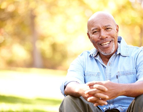 Man in denim shirt sitting outside clasping hands smiling