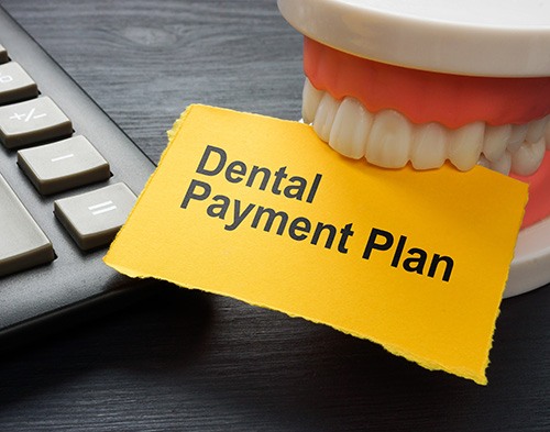 Lower arch of dentures on hundred dollar bills next to dental instruments on a desk